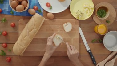 Genç Asyalı kadın şef evdeki mutfak masasındaki tahta tahtaya metal bıçakla çavdar ekmeğine tereyağı sürdü. Taze ev yapımı ekmek üretimi, sağlıklı yemek ve geleneksel fırın. Üst görüntü görüntüsü.