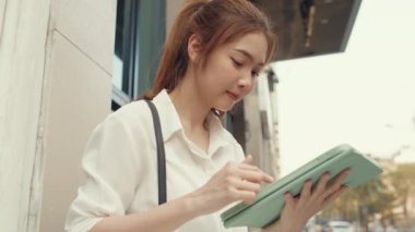 Moda bürosu kıyafetleri içinde başarılı genç Asyalı iş kadını dijital tablet kullanıyor ve sabahları şehir merkezinde tek başına otururken kısa mesaj yazıyor. İş konsepti..