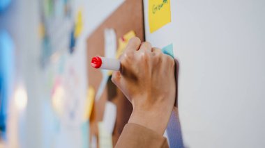 Bir grup genç Asyalı iş adamı iş görüşmelerini tartışıyor birlikte çalışıyor verileri paylaşıyor ve gece ofisindeki yapışkan notla duvara yazı yazıyor. İş arkadaşı takım çalışması konsepti.