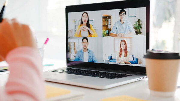 Young Asia businesswoman using laptop talk to colleague about plan in video call meeting while work from home at living room. Self-isolation, social distancing, quarantine for corona virus prevention.