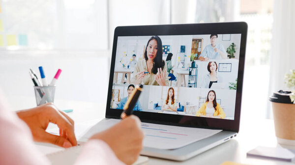 Young Asia businesswoman using laptop talk to colleague about plan in video call meeting while work from home at living room. Self-isolation, social distancing, quarantine for corona virus prevention.