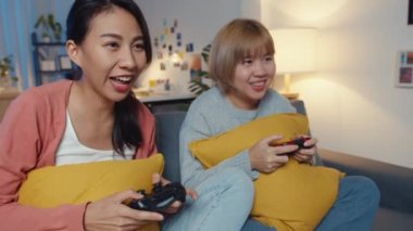 Lezbiyen LGBTQ kadın çifti evde video oyunu oynuyor. Genç Asyalı bayan kablosuz kontrolör kullanıyor. Geceleri oturma odasındaki kanepede mutlu anlar yaşıyor. Tatili kutlamak için harika ve eğlenceli vakit geçiriyorlar..