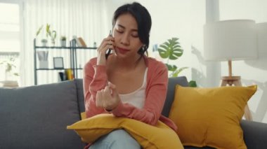 Genç Asyalı bayan kanepede oturup arkadaşlarıyla konuşuyor ve evde kötü haberler alıyor. Uzak mesafe ilişkisi, kötü ilişki, iş sorunu, bozuk ilişki, mesafeyi koru, karantina kavramı.