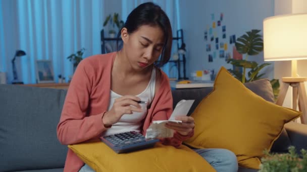アジアの女性は 夜に自宅のソファでお金を計算する請求書や請求書のクレジットカードで心配ストレスを感じる 住宅ローンのストレス ローンを取得しません仕事 コロナウイルスの苦難のローン 支払いの概念を作ることができません — ストック動画