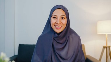 Asyalı müslüman kadın bilgisayarlı dizüstü bilgisayar kullanarak tesettüre giriyor. Video görüşmesi hakkında meslektaşıyla konuşuyor. Evde oturma odasında uzaktan çalışırken. Corona virüsü için sosyal uzaklık, karantina.