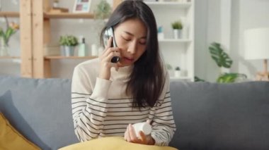 Hasta, genç Asyalı kadın, tıbbı bırakma kanepeye otur ve evdeki doktora danışmak için akıllı telefon kullan. Kız doktordan sonra ilaç alıyor, evde karantina, sosyal mesafeli koronavirüs konsepti..