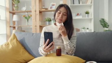 Hasta, genç Asyalı kadın doktorla telefonda konuşurken kanepede otur. Kız doktordan sonra ilaç alıyor, evde karantina, sosyal mesafeli koronavirüs konsepti..