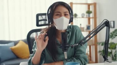 Genç Asyalı kız podcast 'i kulaklık ve mikrofon maskesi kullanıyor. Virüsü koruyor. Odasındaki kamera konuşmalarına bakın. Kadın podcaster kendi stüdyosundan ses yayını yapıyor. Ev konseptinde kalın..