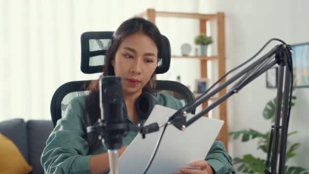 魅力的なアジアの女の子のレコードポッドキャストは 彼女の部屋でオーディオブログの話やレビューのトピックのための練習のためのコンテンツを作成するマイクを保持紙を使用しています 自宅からオーディオポッドキャストを作る 音響機器の概念 — ストック動画