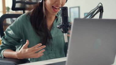 Mutlu Asyalı kız laptopuna kulaklıkla bir podcast kaydediyor ve odasında seyirciyle mikrofon konuşması yapıyor. Kadın podcaster kendi stüdyosundan ses yayını yapıyor. Ev konseptinde kalın..