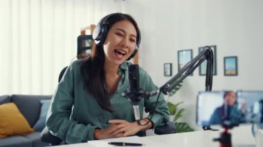 Genç Asyalı kız nüfuzlu biri mikrofon takıyor kulaklık takıyor ve internetteki izleyiciler için akıllı telefonlar çalıyor. Öğrenci kadın podcaster kendi stüdyosundan ses yayını yapıyor..