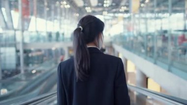 Asyalı iş kızı yüz maskesi takıyor yürüyen merdivenin üzerinde duruyor uluslararası havaalanındaki terminale doğru yürüyor. İş seyahati covid salgını, iş seyahati sosyal uzaklık kavramı.