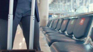 Asyalı iş kadını seyahat eden bayan bavulla oturan takım elbiseli ve bankta akıllı telefon sohbet mesajı kullanarak havaalanında uçuşu bekliyor. İş seyahati gezisi salgını, iş seyahati konsepti.