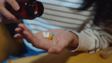 Hap tutan hasta Asyalı genç bayan. İlaca bak. Evdeki kanepede otur. Doktor siparişi üzerine ilaç alan bir kız, evde karantina, Coronavirus sosyal uzaklık sağlık konsepti..