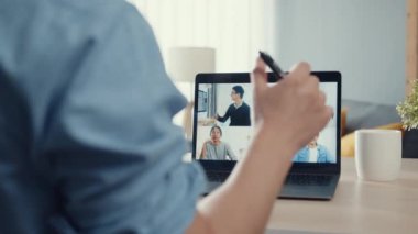 Genç Asya 'lı iş adamı, iş yerinde evden oturma odasına geçerken iş arkadaşlarıyla görüntülü görüşme planları hakkında konuşuyor. Kişisel izolasyon, sosyal uzaklık, korona virüsünün önlenmesi için karantina.