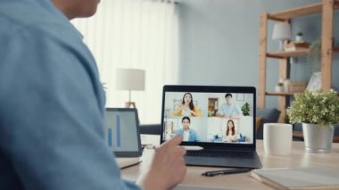 Genç Asya 'lı iş adamı, iş yerinde evden oturma odasına geçerken iş arkadaşlarıyla görüntülü görüşme planları hakkında konuşuyor. Kişisel izolasyon, sosyal uzaklık, korona virüsünün önlenmesi için karantina.