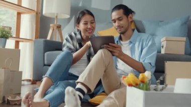 Mutlu Asyalı genç ve çekici erkek ve kadın yeni evlerinde taşınan karton paketlerle ev dekorasyonu yapan tablet alışveriş mobilyaları kullanıyorlar. Genç evli Asyalı eve internetten alışveriş yapıyor..