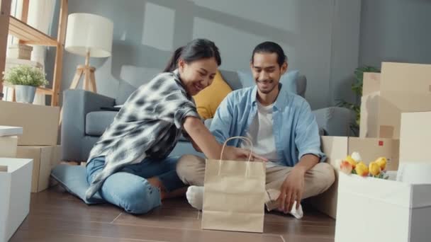 快乐的亚洲年轻貌美的夫妻坐在新家喝咖啡放松 和纸盒一起谈笑风生搬进新家 年轻的亚洲已婚人士搬回家的概念 — 图库视频影像
