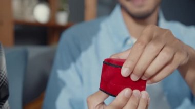 Mutlu Asyalı çift, gülümseyen sevgili kanepeye oturur ve kırmızı kutuda nişan yüzüğüyle sürpriz bir kız arkadaş yapar. Evlenme teklifini evde sorarsın. Yıldönümü romantik kavramı.