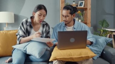 Asya 'lı genç çift kanepede oturur dizüstü bilgisayara bakar evrakları kontrol eder faturaları internetten öder oturma odasında bütçe masrafları öder. Genç evli Asya borç sorunu kavramı.