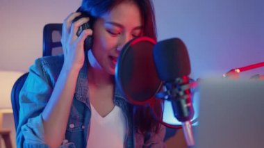 Mutlu Asyalı kız blogger synthesizer klavye çalıyor kulaklık takıyor ve ses mikseriyle birlikte geceleri oturma odasındaki stüdyoda müzik kaydediyor. Müzik içeriği oluşturucu, öğretici, yayın konsepti.