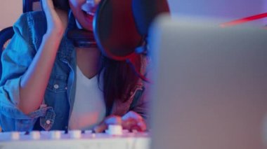 Mutlu Asyalı kız blogger synthesizer klavye çalıyor kulaklık takıyor ve ses mikseriyle birlikte geceleri oturma odasındaki stüdyoda müzik kaydediyor. Müzik içeriği oluşturucu, öğretici, yayın konsepti.