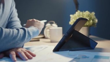 Asya 'nın yakın plan serbest çalışan işadamı tablet bilgisayara, geceleri evde fazla mesai yapan oturma odasında grafikle dolu olan Coronavirus salgını konsepti sırasında evden çalışma.
