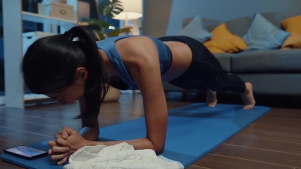 年轻的亚洲女士在运动服练习做运动 并使用电话观看瑜伽视频辅导在家里的夜晚 与个人培训师的远距离培训 社会距离 在线教育概念 — 图库视频影像