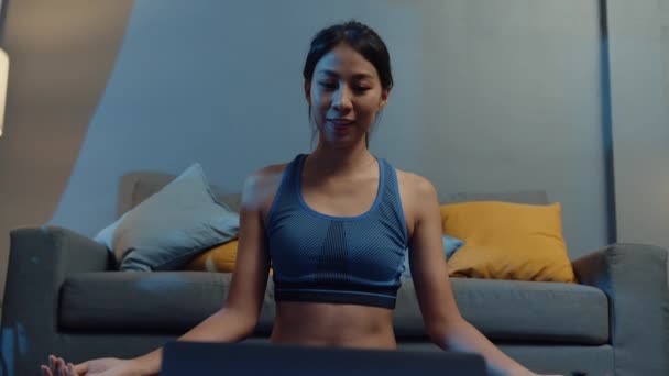 年轻的亚洲女士在运动服练习做运动 并使用笔记本电脑观看瑜伽视频辅导在家里的夜晚 与个人培训师的远距离培训 社会距离 在线教育概念 — 图库视频影像