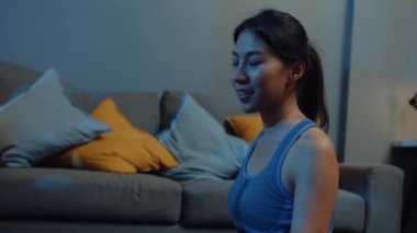 Spor kıyafetli genç Asyalı bayan geceleri oturma odasında yoga egzersizi yapıyor. Spor ve eğlence aktivitesi, sosyal uzaklık, korona virüsü önleme konsepti için karantina.