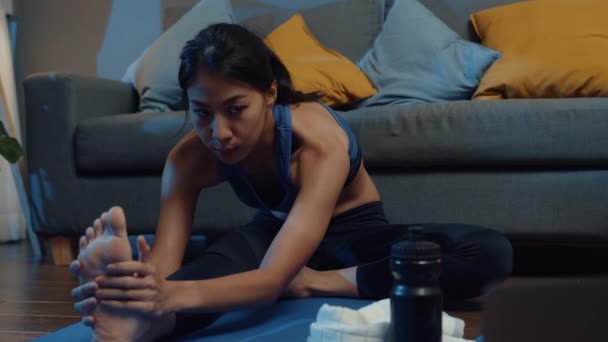 年轻的亚洲女士在运动服练习做运动 并使用笔记本电脑观看瑜伽视频辅导在家里的夜晚 与个人培训师的远距离培训 社会距离 在线教育概念 — 图库视频影像