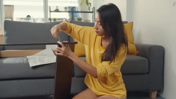 幸せなアジアの若い女性は 箱を開梱し 家庭でのリビングルームでカートンボックス付きの家のビルドテーブルを飾る新しい家具を組み立てるための指示を読んで — ストック動画