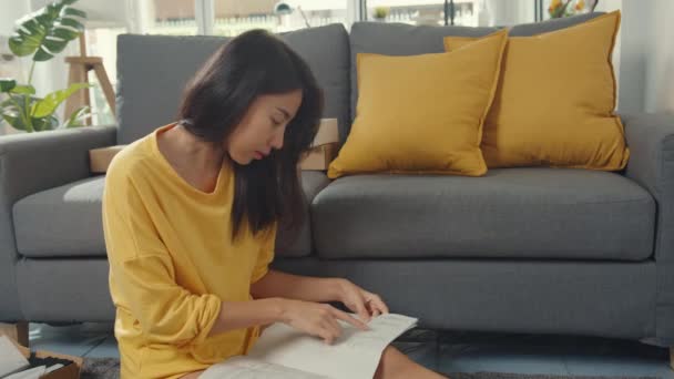 幸せなアジアの若い女性は 箱を開梱し 家庭でのリビングルームでカートンボックス付きの家のビルドテーブルを飾る新しい家具を組み立てるための指示を読んで — ストック動画