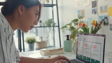 Genç Asyalı bayan serbest olarak dizüstü bilgisayardaki sunum işine ve evdeki şirketle uzaktan görüşme için finans projesine odaklanıyor. Kız öğrenci evde online öğreniyor. Ev kavramından çalış.