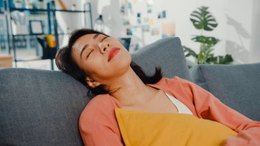 Güzel Asyalı bayan kendini evinde yastıkla kanepede rahatlamış hissediyor. Evde kal, işe ara ver, evinde rahatla, biraz dinlen, mesafeni koru, karantina kavramı..