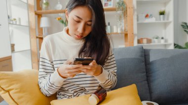 Hasta, genç Asyalı kadın, elinde ilaç tutarken kanepeye otur ve doktoruna fotoğrafını çek. Kız doktordan sonra ilaç alıyor, evde karantina, Coronavirus sosyal mesafeli karantina konsepti..