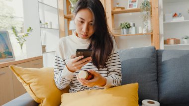 Hasta, genç Asyalı kadın, elinde ilaç tutarken kanepeye otur ve doktoruna fotoğrafını çek. Kız doktordan sonra ilaç alıyor, evde karantina, Coronavirus sosyal mesafeli karantina konsepti..