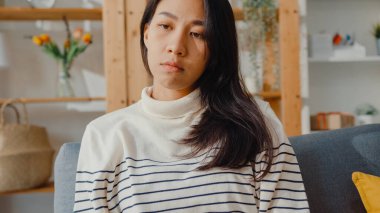 Düşünceli Asyalı kadın oturma odasında dizlerini kucaklayarak oturur kendini yalnız hisseder, üzgün genç kız evde yalnız vakit geçirir, sosyal mesafe, Coronavirüs karantinası..