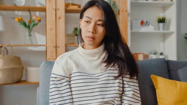 Düşünceli Asyalı kadın oturma odasında dizlerini kucaklayarak oturur kendini yalnız hisseder, üzgün genç kız evde yalnız vakit geçirir, sosyal mesafe, Coronavirüs karantinası..