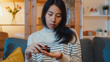 Hap tutan hasta Asyalı genç bayan. İlaca bak. Evdeki kanepede otur. Doktor siparişi üzerine ilaç alan bir kız, evde karantina, Coronavirus sosyal uzaklık sağlık konsepti..