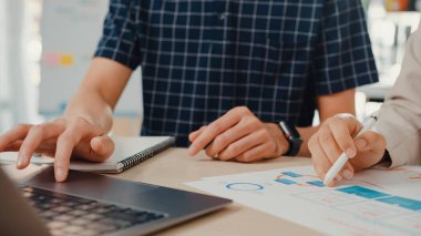 Yakın plan genç iş arkadaşı Asya yaratıcı iş adamı ve iş kadını konuşuyor dizüstü bilgisayardaki proje raporlarını masa başı işleri ve çalışma masasındaki iletişim grafikleriyle karşılaştırın.