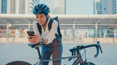 Sırt çantalı gülümseyen Asyalı iş kadını akıllı telefon kamerası kullanıyor. Sokak ortasında bisikletli kamera var. Ofise gidiyor. Spor kızı iş için telefon kullanıyor. İşe gidip gelmek, şehirde iş seyahati yapmak..