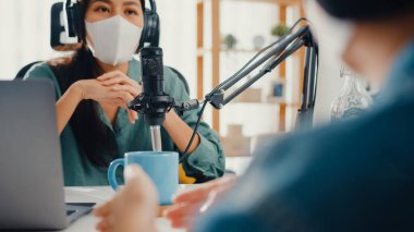 Asyalı kız radyo sunucusu podcast mikrofon takıyor kulaklık takıyor misafir içeriği maske takıyor virüs muhabbetini koruyor ve odasında dinliyor. Evden podcast, koronavirüs karantinası.