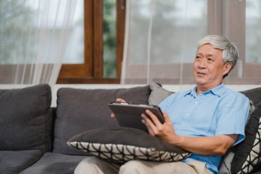 Asyalı son sınıf öğrencileri evde tablet kullanıyor. Asya 'lı üst düzey Çinli erkek ev kavramının oturma odasında kanepede yatarken internette sağlığın nasıl düzeltileceğini araştırıyor..
