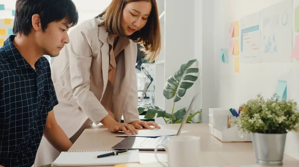 Group of young asia creative businessman and businesswoman team discuss project compare point in paperwork and laptop on table working and communicating together sitting on office desk at workplace.