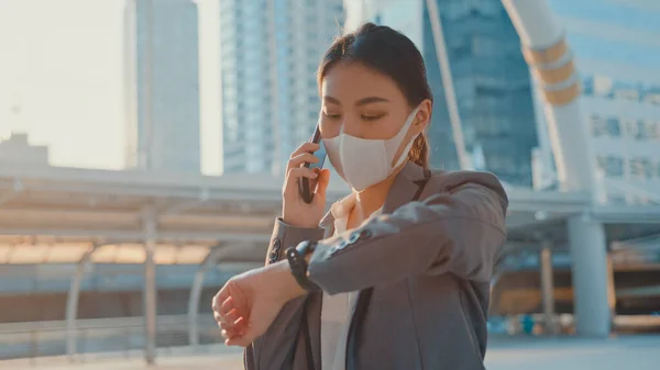 Young Asia businesswoman in fashion office clothe wear medical face mask talk via phone while walk alone outdoor in urban city. Business on go, Social distancing to prevent spread of COVID-19 concept.