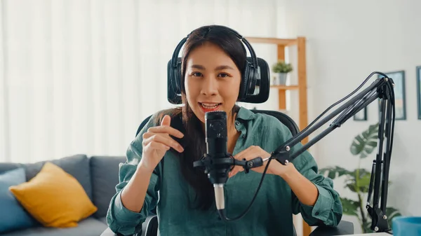 Happy asia girl record a podcast with headphones and microphone look at camera  talk and take a rest in her room. Female podcaster make audio podcast from her home studio, Stay at house concept.
