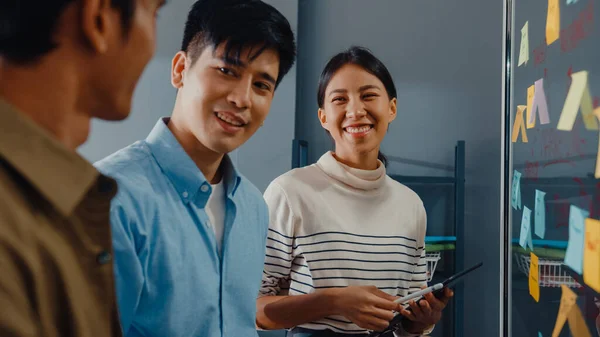 Asia businesspeople stand behind transparent glass wall listen manager pointing progress work and brainstorm meeting and worker post sticky note on wall at office. Business inspiration, Share ideas.