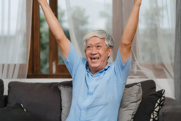 Asian senior men play games at home. Asian senior older Chinese male happy fun and virtual reality, VR playing games while lying sofa in living room at home concept.