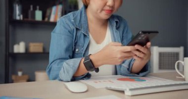 Serbest çalışan Asyalı kadın, oturma odasında masa başında otururken internet üzerinden akıllı telefon alışverişi yapıyor. Evden çalışmak, uzaktan çalışmak, sosyal mesafeler, koronavirüs için karantina.